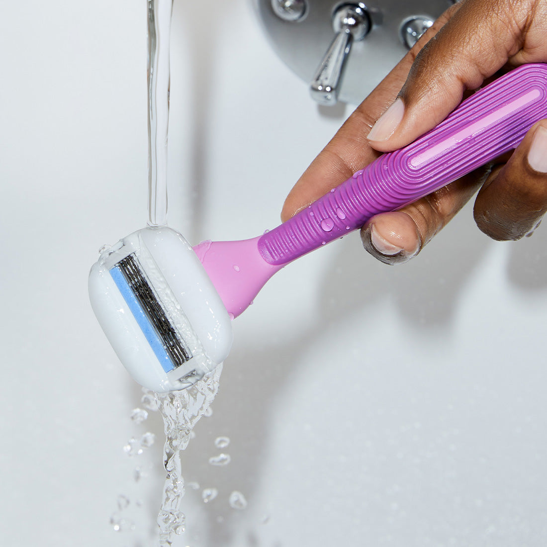 Person rinsing the blades on the Fig Moisture Plus Razor under a stream of water from a bath faucet.