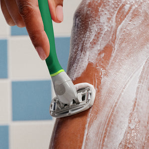 Close up of the green razor shaving a leg lathered with shave gel.