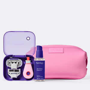 Travel Razor with purple case opened and mini shave oil next to pink Dagne Dover travel pouch on a white background.