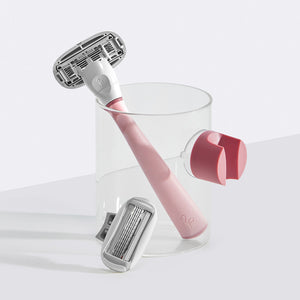 Rose Razor resting in a small glass cup with the shower holder suctioned on the side.