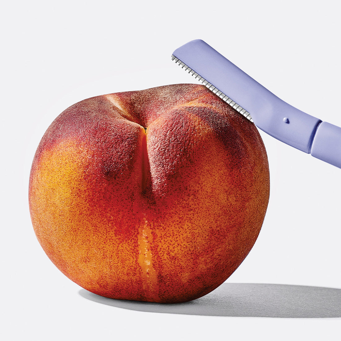 Dermaplane blade resting atop a peach.