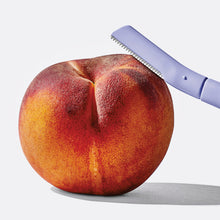 Dermaplane blade resting atop a peach.