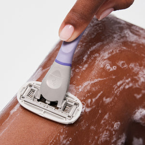 Person using the shave oil and the lilac razor to shave their leg.