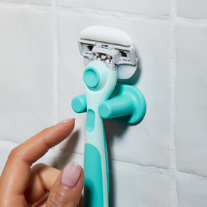 Hand grasping the Sea Foam Moisture Plus razor in its holder on tiled shower wall.