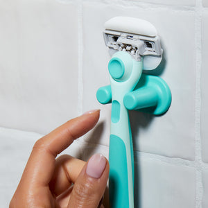 Hand grasping the Sea Foam Moisture Plus razor in its holder on tiled shower wall.
