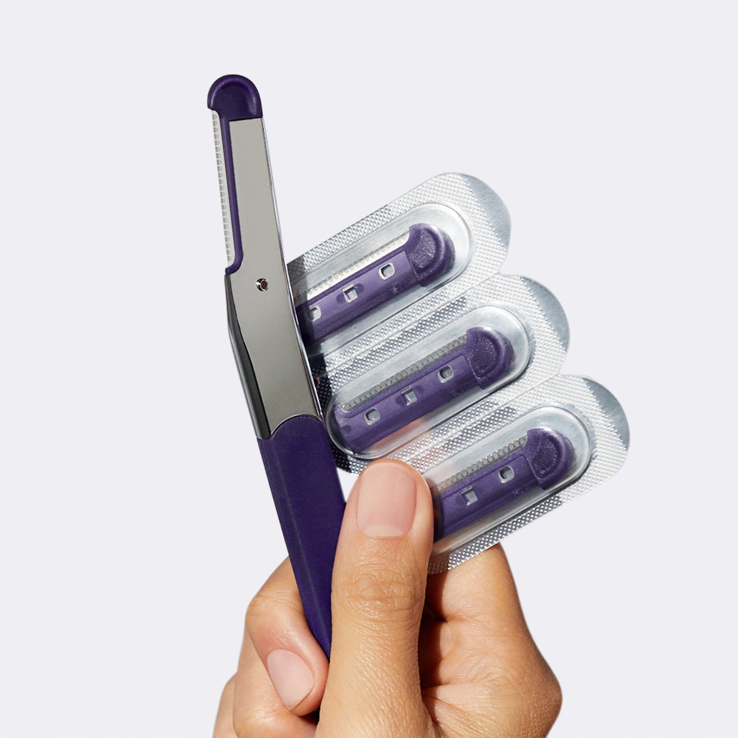 Woman's hand holding up the Flamingo Refillable Dermaplane Razor with three refill blades, each in their own foil pack