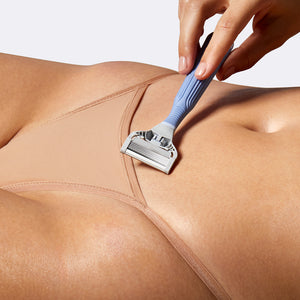 Person holding the Pubic Razor, blade side up, against the skin of their stomach, above their underwear.