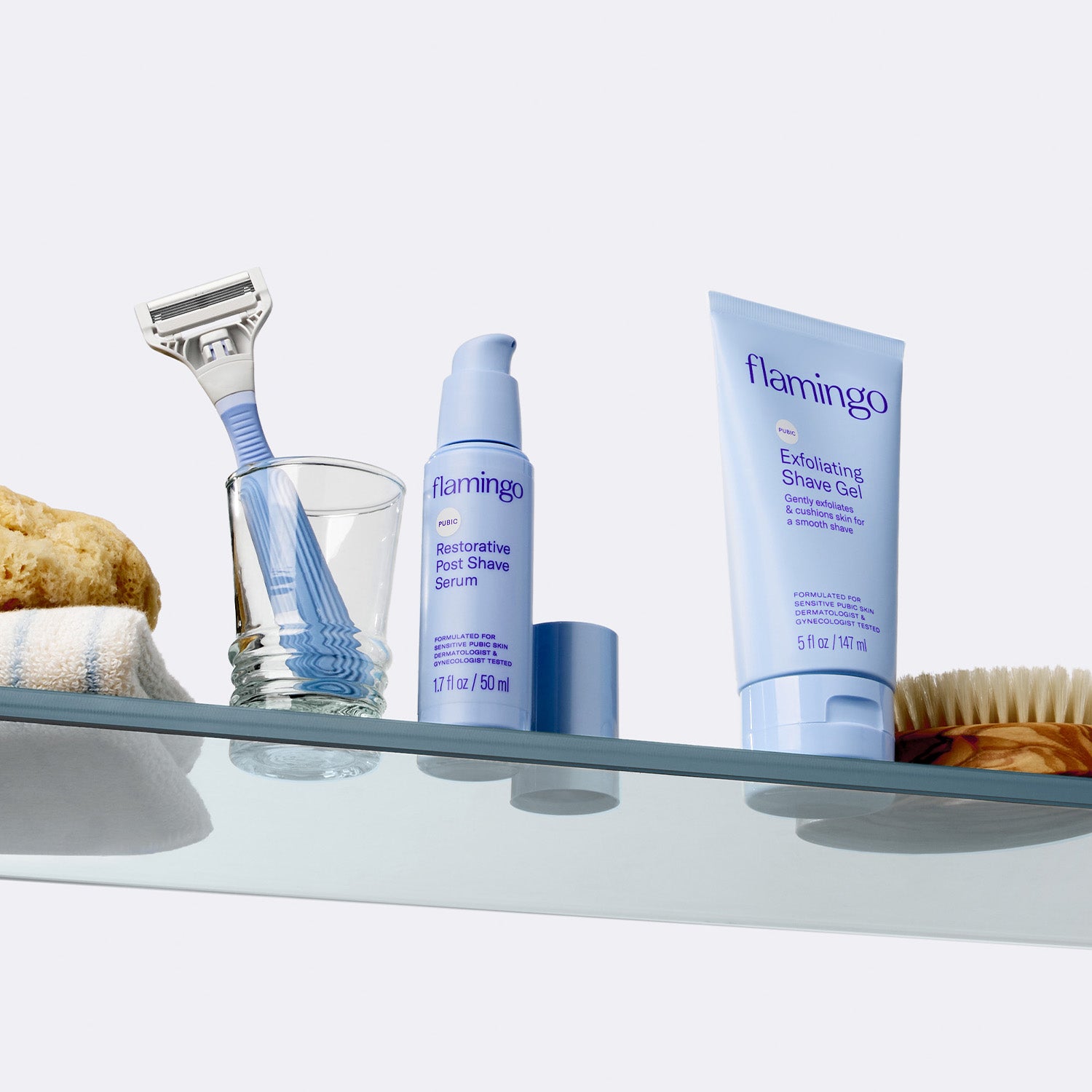 Flamingo's pubic razor, clear shave gel, and post-shave serum pictured on a glass shelf