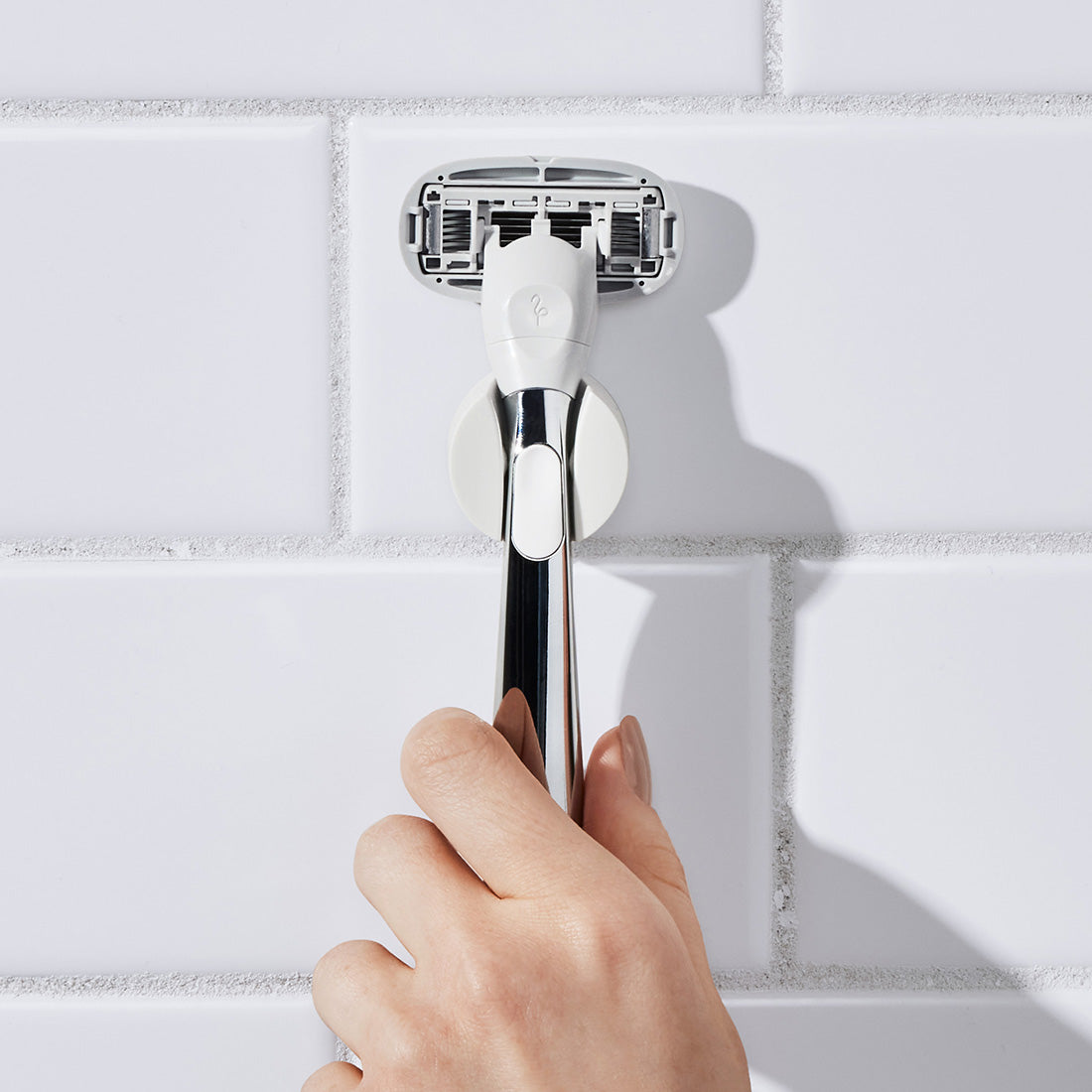 Hand placing the Chrome Razor back into its shower holder.