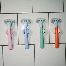 Original Razors in their shower holders on a white tile wall.