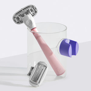 Rose Razor resting in a small glass cup with the lilac shower holder suctioned on the side.