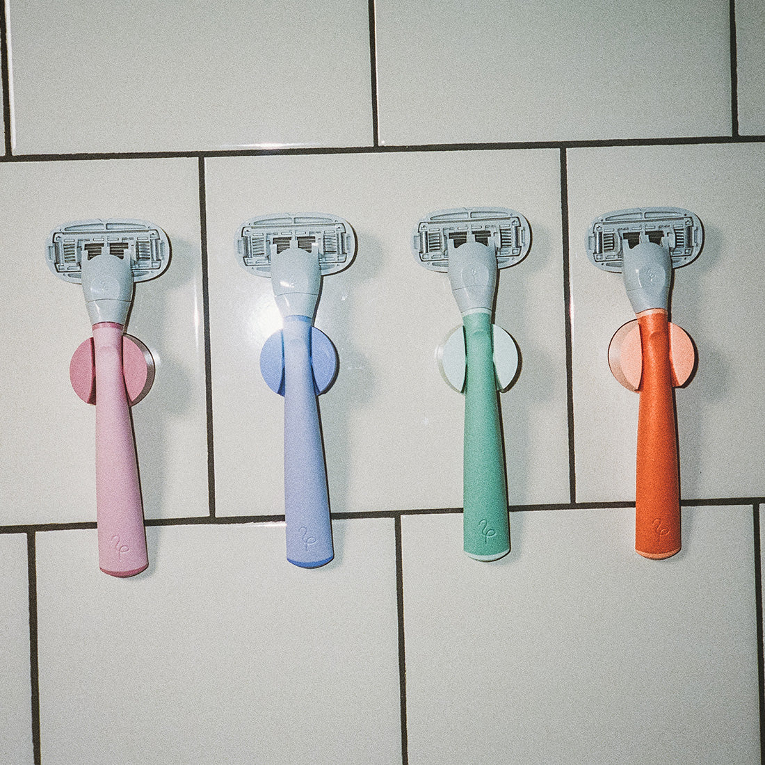 Original Razors in their shower holders on a white tile wall.