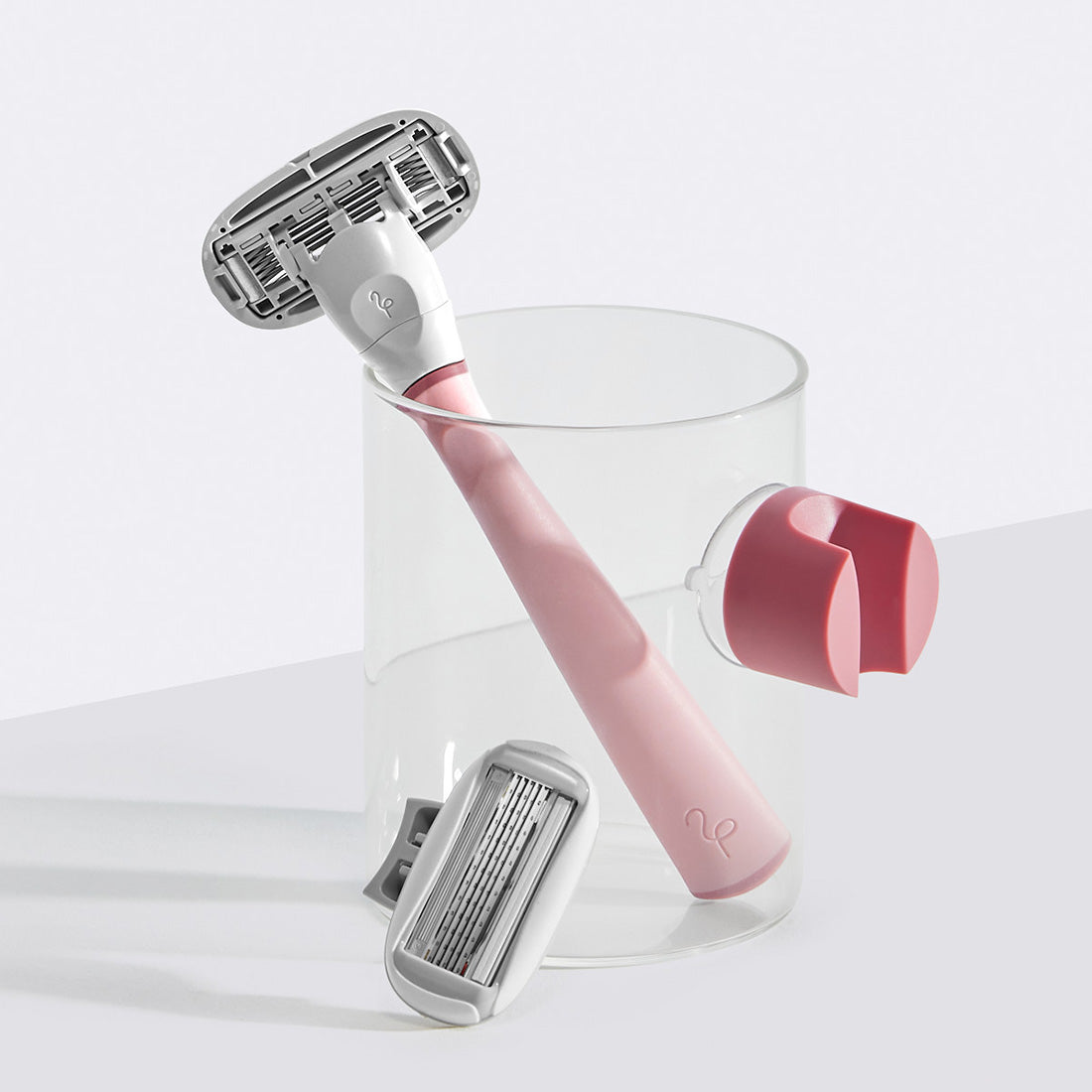 Rose Razor resting in a small glass cup with the shower holder suctioned on the side.