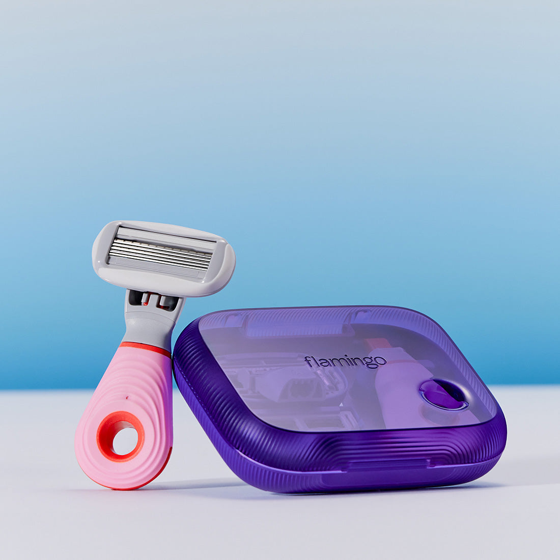 Pink mini razor resting next to the purple plastic case on a light blue background.