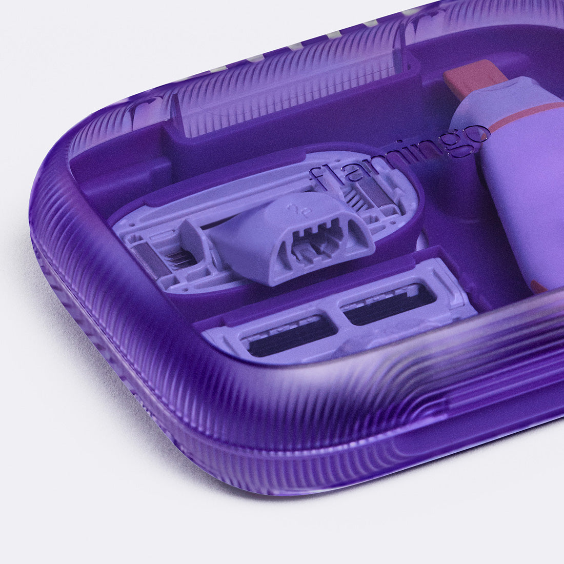Close up of the see through purple plastic travel case holding an Original blade, Pubic blade and the mini travel handle.
