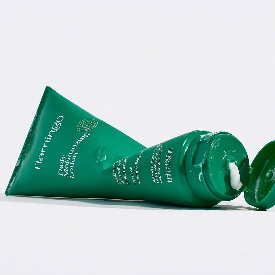 Green tube of Flamingo Daily Moisturizing Lotion pictured sideways and squeezed like it has just been used