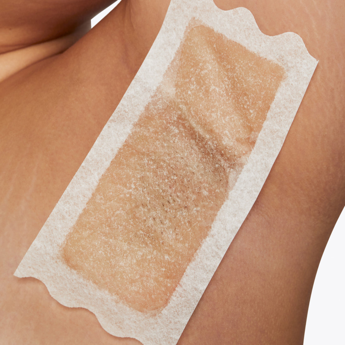 Closeup of a woman's armpit with a large Flamingo Wax strip applied