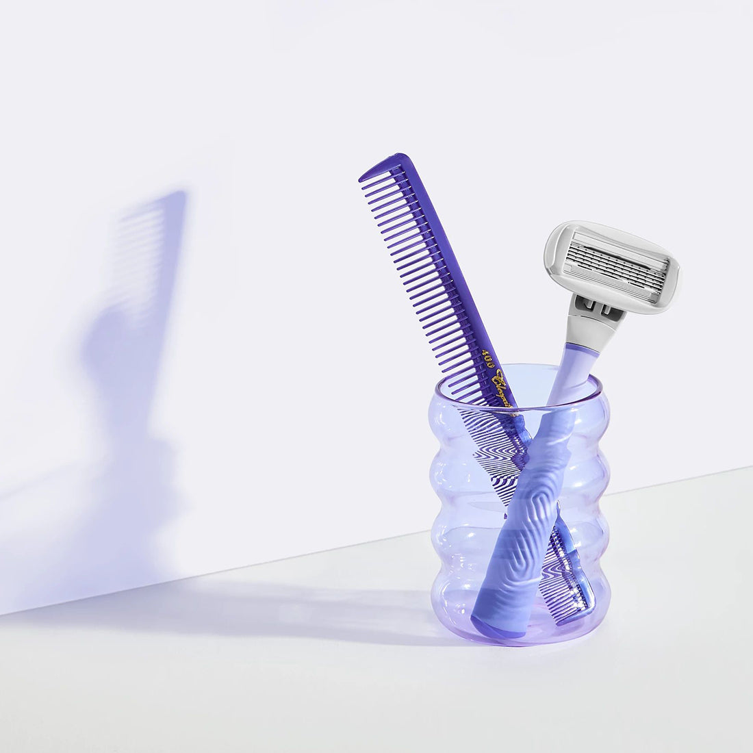 Flamingo Lilac Razor in a funky purple clear glass cup that also contains a dark purple comb
