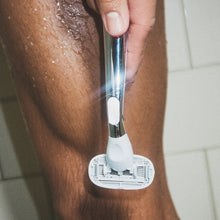 Closeup of a person holding a Flamingo Polished Chrome Razor in front of their leg in the bathroom