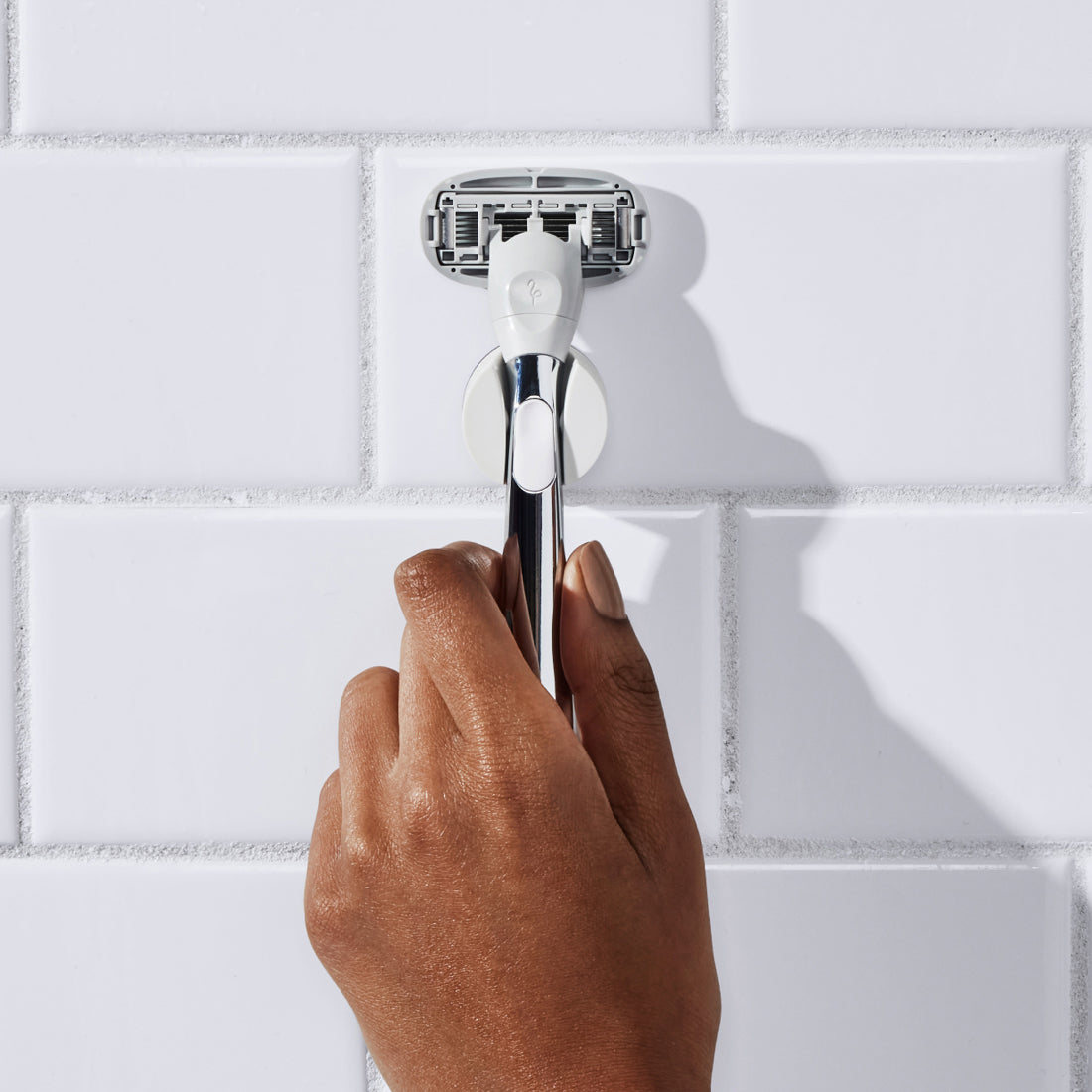 Woman removing the Polished Chrome Flamingo Razor from its shower holder on a white bathroom wall
