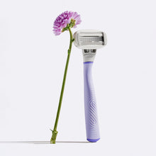 Flamingo Razor in the color Lilac leaning up against a purple flower with a long green stem