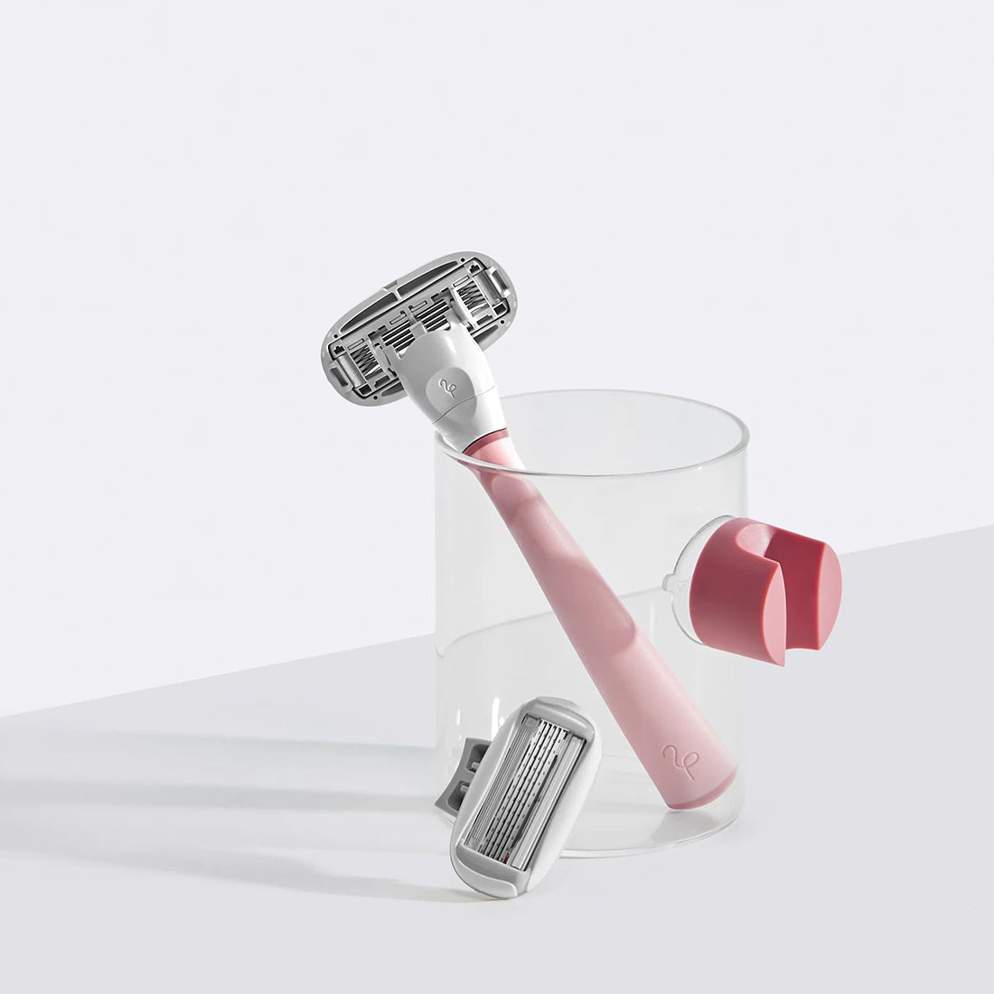 Rose Flamingo razor in a glass cup with a blade cartridge on the side and the rose shower holder suctioned to the cup