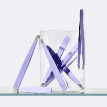 Eight pairs of lilac Flamingo Tweezers arranged in and around a small glass beaker